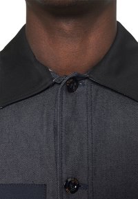 Denim shirt with a dark navy collar, featuring contrasting stitching and a G-Star button at the neck. Close-up view of collar and fabric texture.