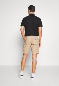 Polo noir avec col, assorti à un short beige. Le short a des poches arrière et arrive au genou. Des baskets blanches complètent la tenue.