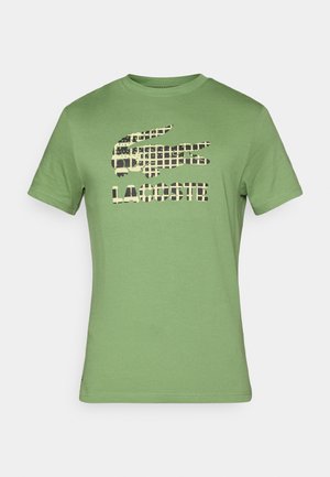 Green short-sleeve t-shirt made of cotton, featuring a black and tan crocodile logo and "LACOSTE" text printed on the front.