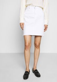 Bílá denimová sukně s jednoduchým designem, délky do poloviny stehna, se zapínáním na knoflík a zip. Spárováno s černými loafery.