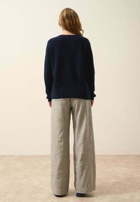 Granatowy sweter dziany o luźnym kroju, zestawiony z jasnoszarymi spodniami o szerokich nogawkach z delikatną teksturą. Ubranie widoczne z tyłu.