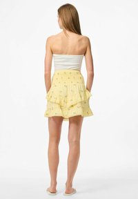 Falda amarilla con capas y patrones florales, con un dobladillo con forma de ondas, combinada con una blusa blanca ajustada sin mangas. Textura suave, diseño casual.