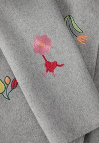 Tessuto grigio con ricami floreali. Caratterizzato da un fiore rosa, una base a forma di cuore rossa, foglie verdi e accenti arancioni. Superficie morbida e strutturata.