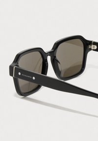 Mustat kooltaan ylisuuret neliöaurinkolasit, joissa on tummat linssit ja paksut sangat. Aurinkolaseissa on 'ALLSAINTS' -brändäys ja heksagoniset yksityiskohdat.