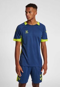 Blauwe sportshirt met gele accenten, korte mouwen en een ronde hals. Heeft textuur op de schouders en een logo aan de voorkant.