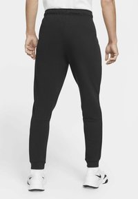 Zwarte sportbroek met een getailleerd ontwerp, elastische tailleband en geribde boorden, gecombineerd met witte sportieve schoenen.
