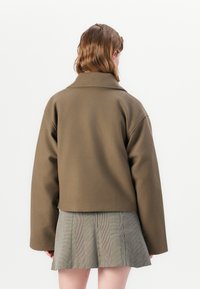 Brown wool-blend jacket with a tailored collar, relaxed fit, and dropped shoulders, paired with a checkered pleated skirt.