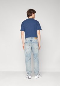 Camiseta de manga corta en color navy combinada con unos jeans de corte relajado en azul claro. Con un ligero desgaste notable y un parche de cuero marrón en la cintura.