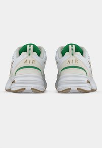 Witte sportschoenen met groene accenten, gewatteerde kraag, gestructureerd materiaal, luchtdemping en gouden "AIR" branding op de hak.