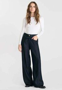 Wijde denim broek in donkerblauw met een hoge taille, voorzakken en een trekkoorddetail. Gecombineerd met een nauwsluitend wit langemouwen top.