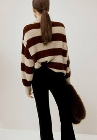 Suéter de punto con amplias franjas marrones y beiges, con hombreras caídas. Combina con pantalones negros y un accesorio de piel sintética marrón.