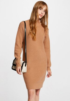 Robe en tricot à manches longues de couleur brun clair avec une texture côtelée. Dotée d'un col montant et d'un tissu doux. Accompagnée d'un petit sac bandoulière crème.