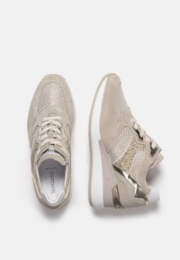 Beige suede sneakers with textured detailing, metallic accents, and a cushioned sole. Laces and a padded collar complete the design.