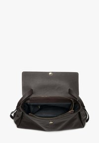 Brązowa skórzana torebka o fakturowanej powierzchni, z otwartą kieszenią na zamek błyskawiczny i zapięciem na magnes. Wnętrze wyściełane ciemną tkaniną.