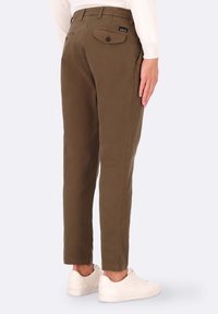 Pantaloni in cotone marrone con vestibilità slim, dotati di tasche laterali e posteriori con bottoni. Indossati con sneakers bianche, che mostrano un orlo pulito.