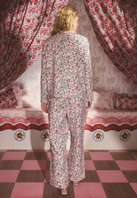 Floral pajama set with a light pink background, featuring red flowers and green leaves. Loose, long sleeves and wide-leg pants. Soft fabric texture.