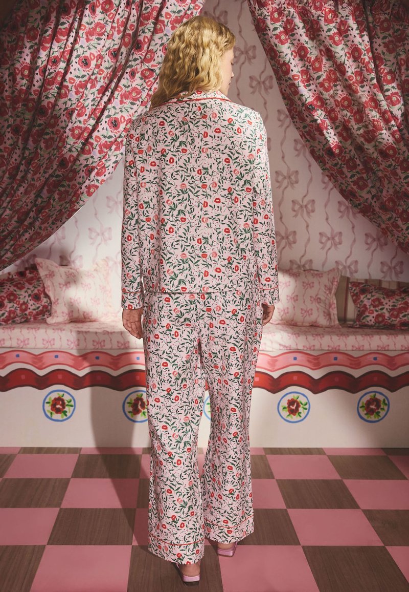 Floral pajama set with a light pink background, featuring red flowers and green leaves. Loose, long sleeves and wide-leg pants. Soft fabric texture.