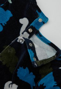 Tissu à motifs floraux bleu et noir avec des boutons-pression. Texture douce avec un col et une doublure intérieure contrastante, comportant des nuances de gris et de vert.