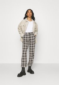 Chaqueta de pana beige, camiseta blanca, pantalones de cuadros en blanco y negro, y botas negras con cordones. Ajuste moderno y diseño estructurado.