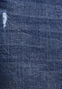 Tela de mezclilla azul oscura con un tejido texturizado, que presenta una zona ligeramente desgastada y un sutil desvanecimiento, indicando uso y un estilo casual.