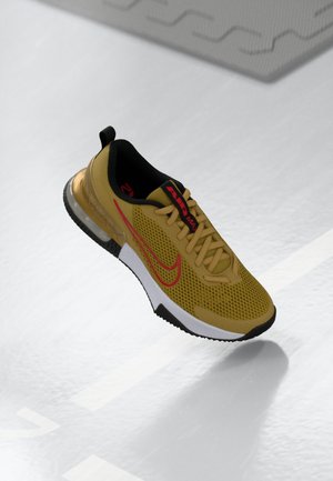 Żółty meshowy sneaker Nike Air Max z czerwonym logo i czarną podeszwą, pokazany unoszący się nad szarą podłogą z cieniem pod spodem.