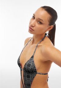 Bikini mustassa ja harmaassa, jossa on kuvioitu design, ja kaksilla kolmionmuotoisilla kupeilla sekä solmittavilla nauhoilla säädettävyyttä varten. Sileä pinta.