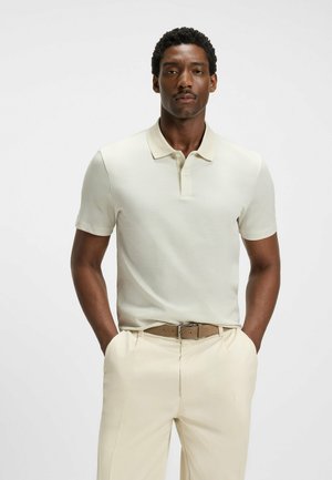 Light beige polo shirt with a textured pattern, short sleeves, and a fold-down collar, paired with light beige trousers and a tan belt.