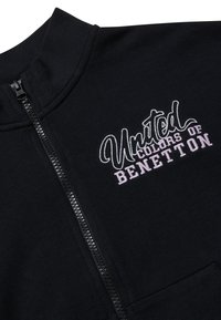 Felpa nera con zip e collo alto, con logo ricamato "United Colors of Benetton" in bianco e rosa. Tessuto morbido, senza motivi.