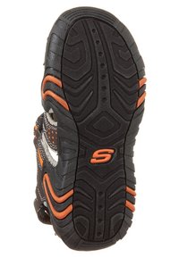 Czarna gumowa podeszwa buta z pomarańczowymi akcentami i teksturowanymi wzorami zapewniającymi przyczepność. Posiada okrągłe i zygzakowate rowki dla lepszej trakcji.