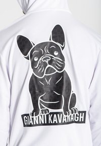 Biela mikina s kapucňou, ktorá má veľký čierno-biely grafický motív francúzskeho buldoga, s nápisom "GIANNI KAVANAGH" vytlačeným pod ním.