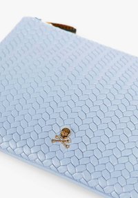 Clutch de piel de color azul claro con textura trenzada y un emblema de calavera y huesos cruzados en dorado. Cierre con cremallera a lo largo del borde superior.