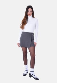 Gonna avvolgente grigia con dettaglio a cintura, abbinata a un dolcevita bianco fitted. La modella indossa scarpe in vernice nere e calze bianche al ginocchio.