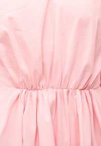 Απαλό ροζ ύφασμα με σούρα στη μέση από ελαστική ταινία, δημιουργώντας απαλές πτυχώσεις και ελαφρώς γυαλιστερή υφή.