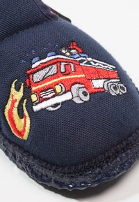 Navyblauwe stoffen slipper met geborduurde rode brandweerwagen met een brandweerman en vlammen, verfraaid met blauwe en gele details.
