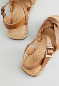 Sandali in pelle marrone con design a fascia incrociata, dettaglio fibbia e suola texturizzata. La soletta interna ha una finitura simile alla scamosciata.