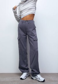 Grå cargo-bukser med flere lommer, en afslappet pasform og lige snit. Bæres med en stribet langærmet bluse.