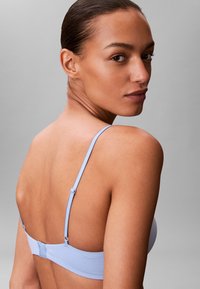 Sujeción azul claro con tirantes ajustables y cierre de gancho. Textura suave con diseño minimalista, mostrando un estilo trasero simple.