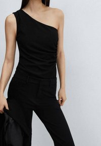 Haut noir à une épaule avec une texture froncée, associé à un pantalon noir sur mesure. Le tissu lisse et la coupe ajustée créent une silhouette élégante.