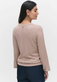 Ljust rosa tröja med långa ärmar, ribbade muddar och en dekorativ knapp bak. Slät textur, åtsittande design, kombinerad med mörk denim.