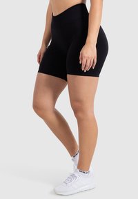 Zwarte high-waisted fietsbroekjes gemaakt van gladde stof, met een strakke pasvorm en naadloze constructie voor comfort. Gecombineerd met witte sneakers.