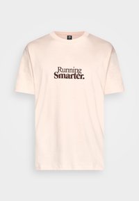 Camiseta de algodón rosa claro con mangas cortas y cuello redondo. En la parte frontal se muestra el texto "Running Smarter." en letras marrón oscuro.
