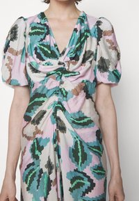 Mujer que lleva un vestido de patrón abstracto colorido con mangas cortas abullonadas y un detalle retorcido fruncido en el pecho y la cintura.