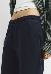 Marinefarbene Jogginghosen mit elastischem Bund, Kordelzug, Seitentaschen und kleinem Logodetail. Kombiniert mit einem karierten Hemd.