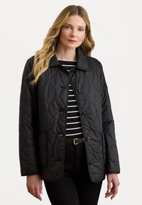 Veste matelassée noire avec un col, un devant à boutons et des poches latérales, portée sur un haut à rayures noir et blanc. Texture lisse.