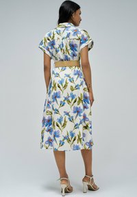 Vestido midi floral con mangas cortas, tejido blanco cubierto de flores azules y verdes, ceñido a la cintura con un cinturón trenzado.