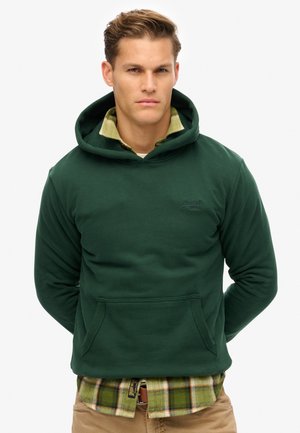 Groene hoodie van zachte stof met een kangoeroezak, gelaagd over een geruit groen en geel shirt. Heeft een geborduurd logo op de borst.