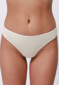 Alacsony derekú, krémszínű, pamut bikini alsónemű, sima textúrával, oldalsó varrásokkal és minimális elasztikus részletekkel a deréknál.