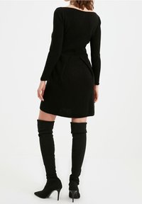 Black knit dress with long sleeves and a fitted bodice, featuring a flared hem. Paired with thigh-high black boots and matching heels.