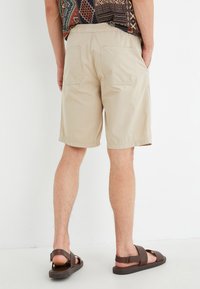 Pantalones cortos beige de tela ligera, con un corte relajado, dos bolsillos traseros y combinados con sandalias marrones.