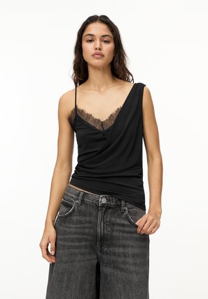 Black top with lace trim at the neckline, featuring an asymmetrical design and one shoulder strap, paired with dark gray denim pants.
